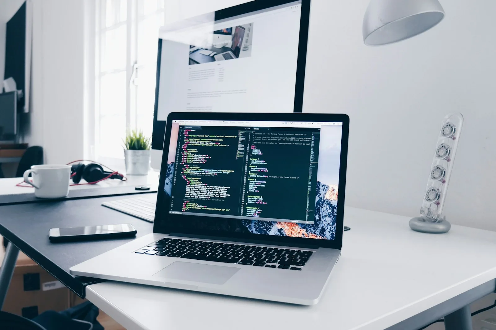 Laptop displaying code on a desk beside a monitor